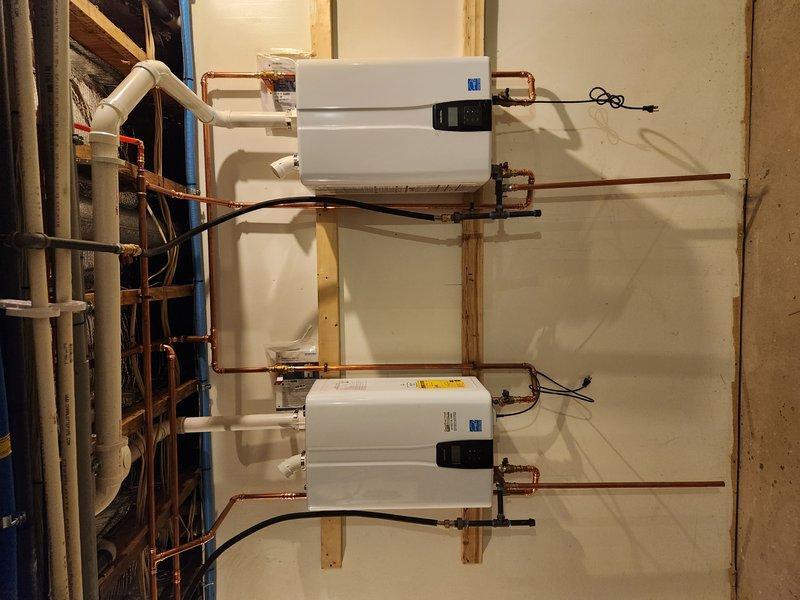 Completed installation of dual Navien NPE240A2 tankless water heaters, relocating one existing unit and adding a second unit to support bathroom remodel. Installed new copper supply lines with press fittings and connected PEX distribution lines for hot and cold water service. Mounted units on wooden support frames with proper venting and electrical connections.