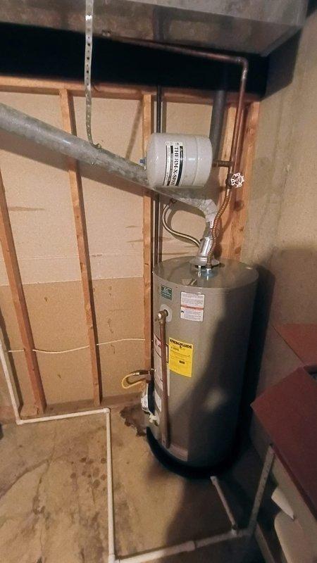 Middlebury, IN - Responded to service call for leaking tanked water heater in residential property. Upon inspection, identified active leak on seven-year-old unit that had been present for multiple days with no resulting water damage to surrounding area. Assessed water heater condition, plumbing connections, expansion tank, and venting system to determine source of leak and verify proper installation standards. Documented equipment configuration including copper supply lines, expansion tank mounting, and exhaust venting in utility room with exposed framing.