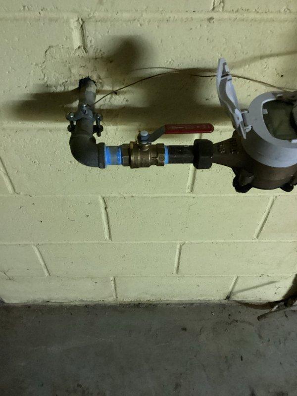 Replaced defective shut-off valve on the main water line before the meter and repaired a leaking copper elbow fitting connected to the water softener supply. Installation included new brass valve with red handle and secure connections to ensure proper water flow and eliminate leaks.