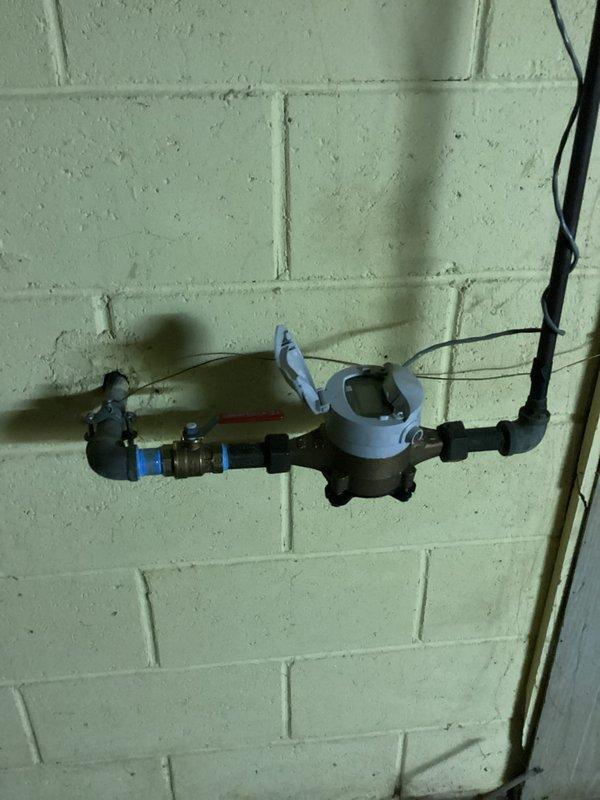 Replaced defective shut-off valve on the main water line before the meter and repaired a leaking copper elbow fitting connected to the water softener supply. Installation included new brass valve with red handle and secure connections to ensure proper water flow and eliminate leaks.