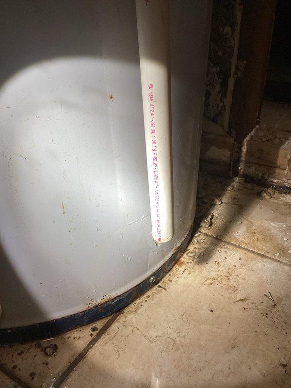 Niles, MI - Inspected 12-year-old non-functioning water heater to verify overflow damage for insurance claim. Confirmed active water leakage from tank with visible water/debris accumulation at base. Documented condition with photographs showing the white cylindrical tank, PVC plumbing connections, and evidence of leakage at the tank's bottom seal.