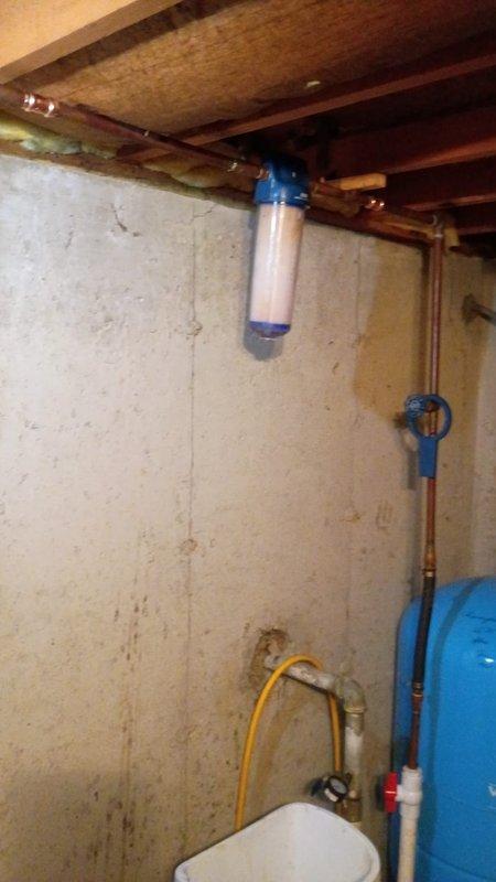 Responded to service call for leaking whole home water filtration system in basement utility area. Upon arrival, inspected cylindrical water filter housing with blue end caps mounted horizontally on wall and connected to copper piping system. Conducted thorough diagnostic evaluation of filter assembly, housing integrity, and all connection points to identify source of leak. Examined pressure tank, associated plumbing connections, and mounting hardware for signs of damage or failure. Assessed condition of filter canister, seals, and O-rings for cracks or deterioration that could cause water intrusion. Documented existing water treatment system configuration including filter housing, copper supply lines, pressure gauge assembly, and blue pressure tank. Provided recommendations for repair or replacement options based on age and condition of equipment that had been installed prior to current homeowner occupancy over thirteen years ago.