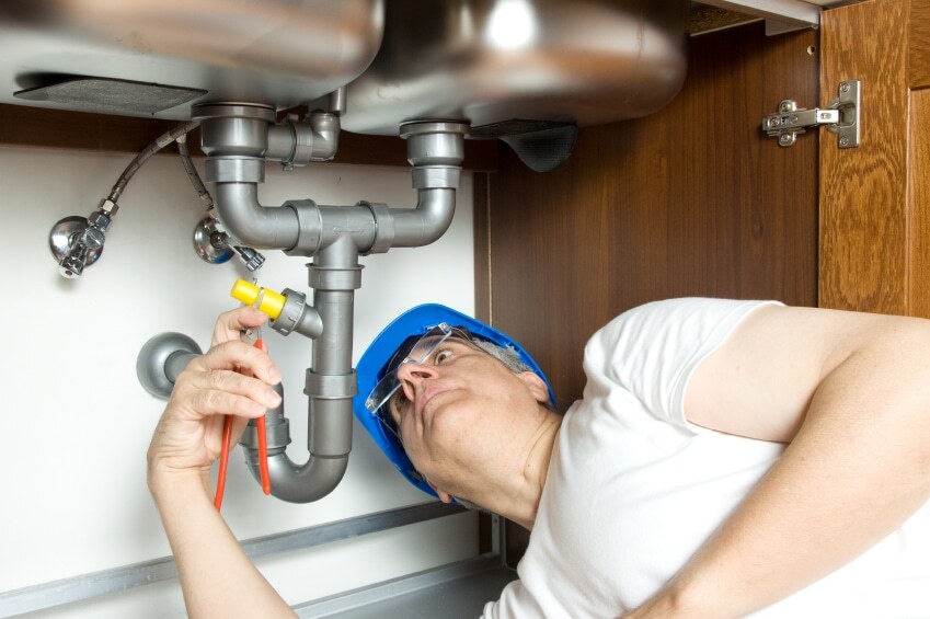plumber under sink with wrench adjusting pipes