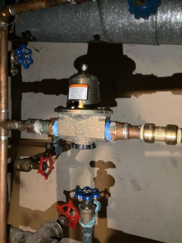 Inspected aging heating system in response to no-heat complaint. Found pressure regulator showing signs of oxidation with multiple shut-off valves in the plumbing installation. Examined the boiler unit with connected copper piping, pressure gauge, and insulated ductwork for proper operation.