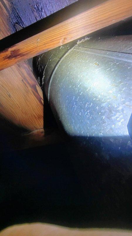 Conducted a site assessment to evaluate the existing chimney system for B-vent replacement. Documented the current installation with detailed photos of both the rooftop brick chimney structure and the attic connection point where wooden joists meet the metal ductwork. Noted signs of possible moisture issues and aging on both the wooden structural elements and the weathered brick chimney exterior.