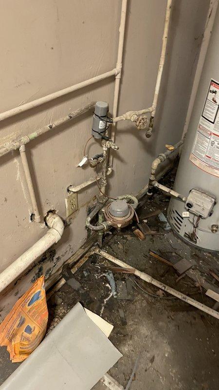 Responded to emergency call for water intrusion in utility area affecting water heater and plumbing infrastructure. Upon arrival, found extensive flooding with contaminated water and debris throughout the space, indicating a significant pipe failure or burst line. Shut off main water supply to prevent further property damage. Assessed plumbing assembly including multiple connection points, valves, and pressure relief components for source of leak. Documented severe water damage to flooring and surrounding area with thick sediment accumulation. Inspected secondary plumbing fixtures including toilet tank which showed signs of water quality issues with discolored water and mineral buildup in fill valve and flush valve assemblies. Cleared immediate water hazard and identified compromised piping requiring replacement. Provided recommendations for water extraction, structural drying, and complete pipe repair to restore system integrity and prevent future failures.